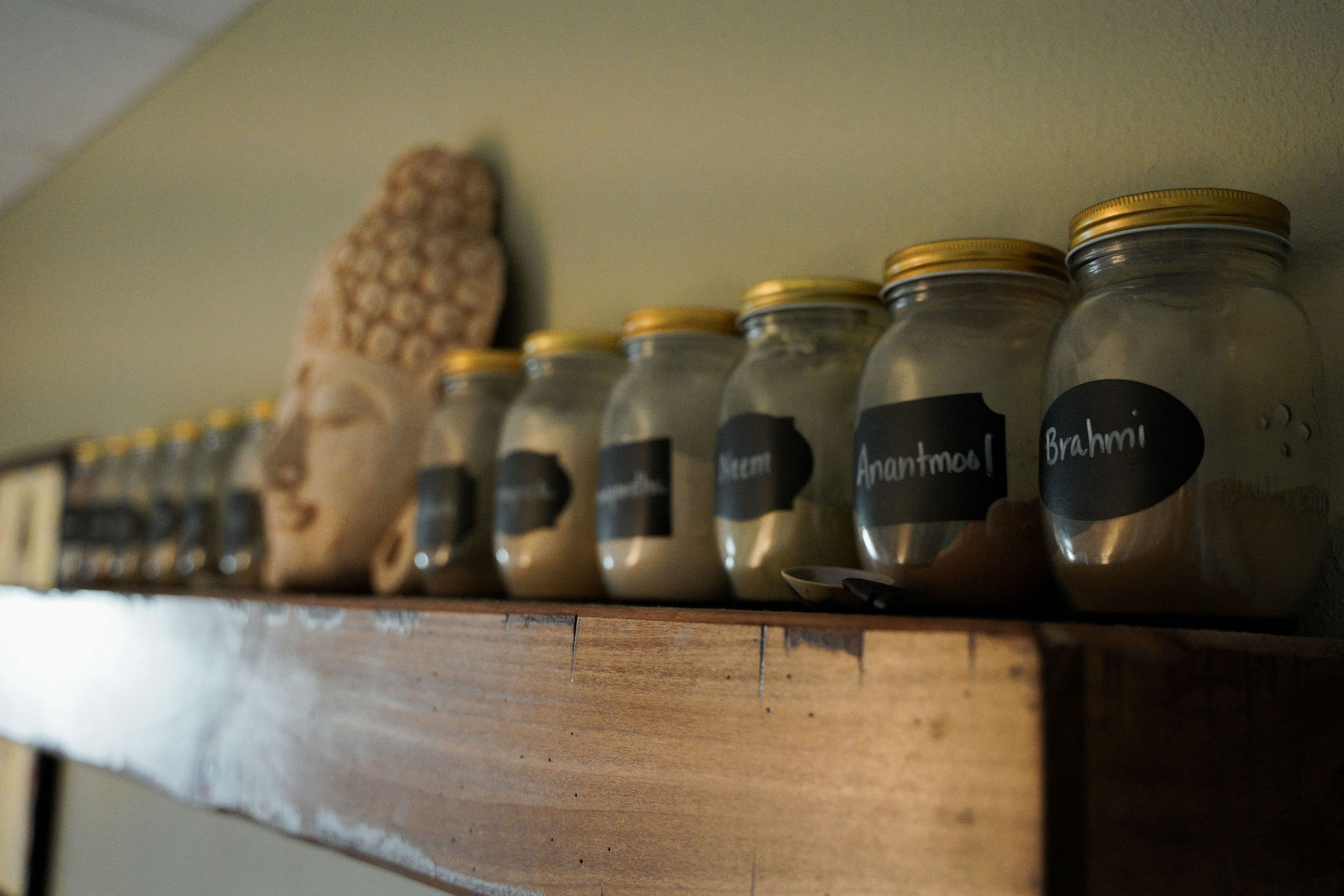 Āyurvedic herbal powders in labelled jars on a wooden shelf