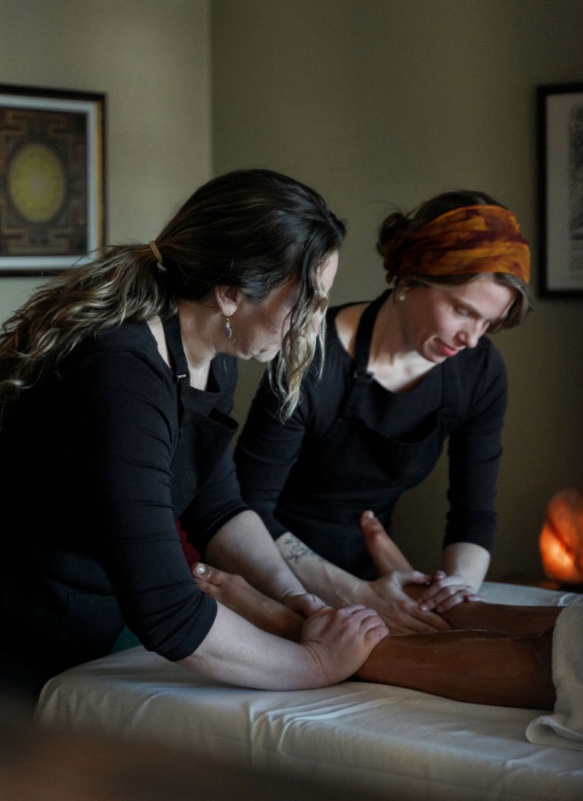 Two practitioners performing an Abhyanga massage treatment with a client